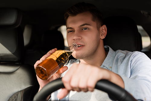 young man drinking whiskey while driving car on blurred foreground