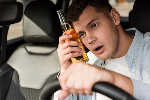 drunk man holding bottle of alcohol near head while driving car on blurred foreground
