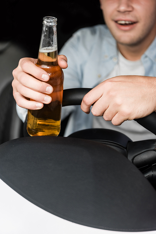 partial view of drunk man holding bottle of whiskey while driving car, blurred background