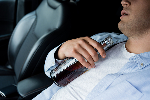 partial view of drunk man sleeping with bottle of alcohol on drivers seat in car