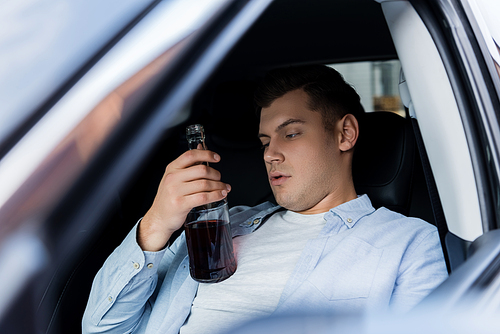 drunk man holding bottle of whiskey while sitting on drivers seat in car