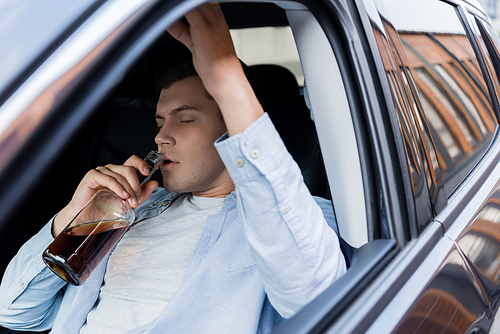 drunk, sleepy man sitting in car and drinking whiskey with closed eyes