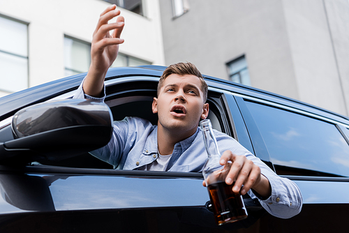 drunk, angry man with bottle of whiskey shouting while looking out car window
