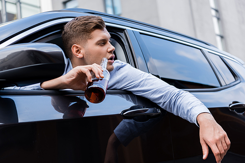 drunk man looking out car window while holding bottle of whiskey