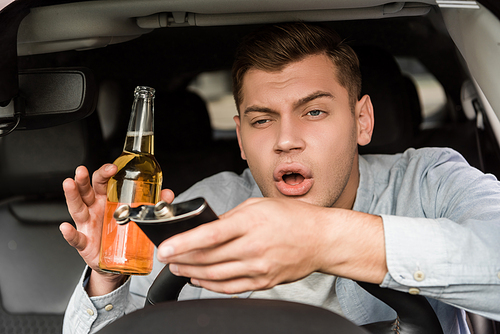 drunk man holding bottle of whiskey and flask while sitting in car