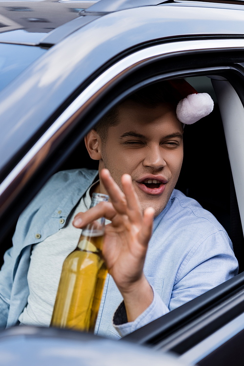 drunk, excited man in santa hat sitting in car with bottle of whiskey on blurred foreground