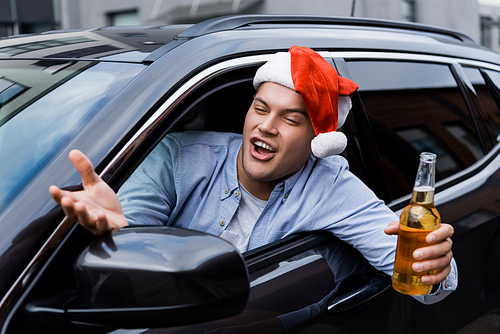 excited, drunk man in santa hat, with flask of alcohol, gesturing while looking out car window