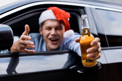drunk man in santa hat  while sitting in car and holding bottle of whiskey in outstretched hand