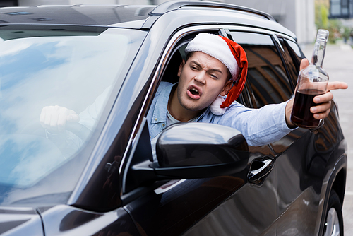 drunk, angry man in santa hat, with bottle of whiskey, looking out window while driving car
