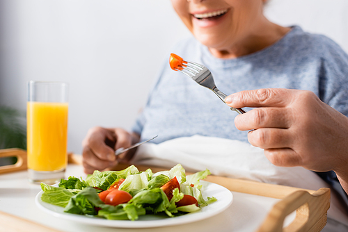 cropped view of joyful woman having breakfast in hospital, blurred background