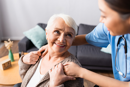 happy elderly woman touching hands of young asian nurse on blurred foreground