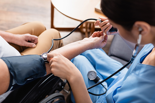 partial view of nurse measuring blood pressure of senior patient, blurred foreground
