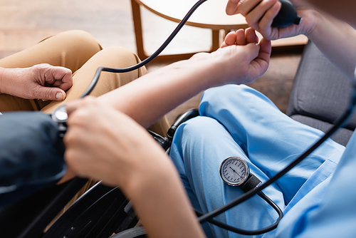 cropped view of nurse measuring blood pressure of elderly woman, blurred foreground