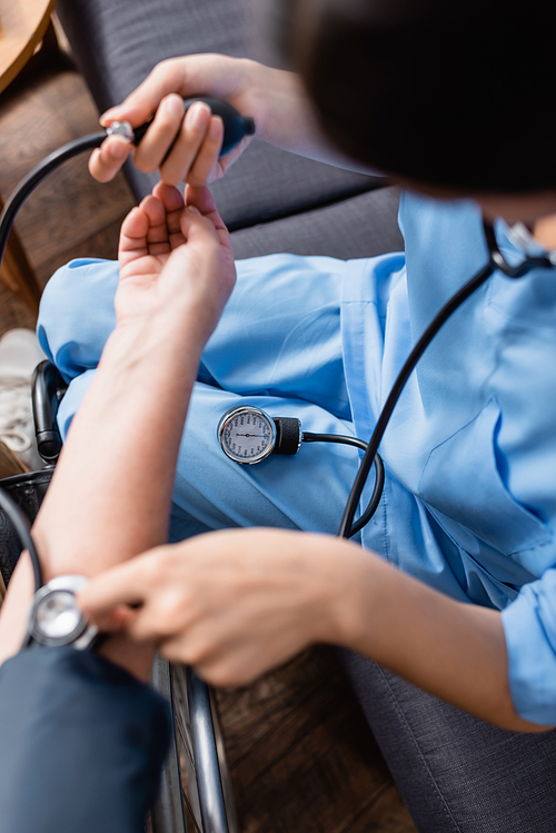 cropped view of nurse measuring blood pressure of senior woman with tonometer, blurred foreground
