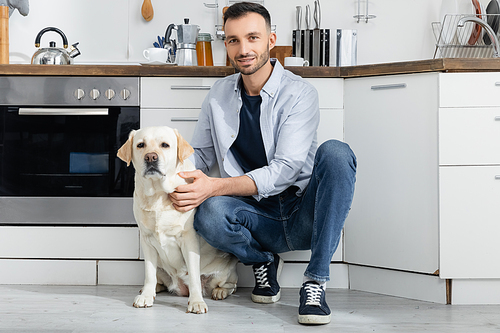 happy man in jeans sitting and cuddling labrador at home
