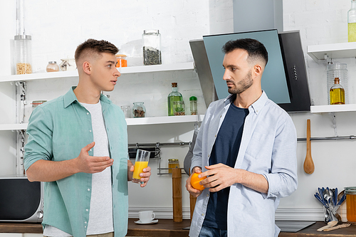 confused homosexual men holding fruit and orange juice in kitchen
