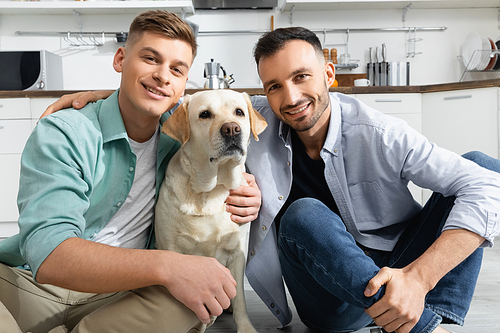 cheerful homosexual men smiling with dog at home