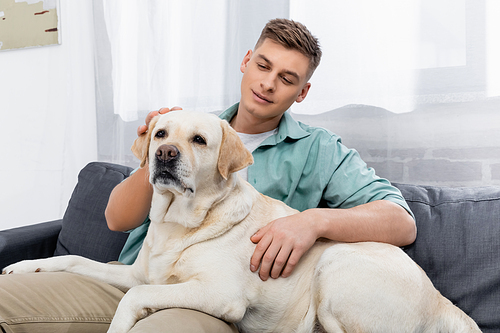 pleased man sitting on couch and cuddling labrador