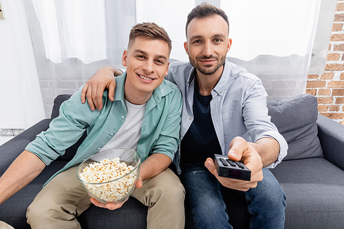 joyful same sex couple watching movie with tasty popcorn