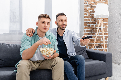cheerful same sex couple watching film with popcorn