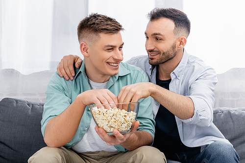 cheerful same sex couple looking at each other while reaching popcorn