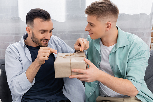 happy homosexual man pulling bow on valentines present near husband