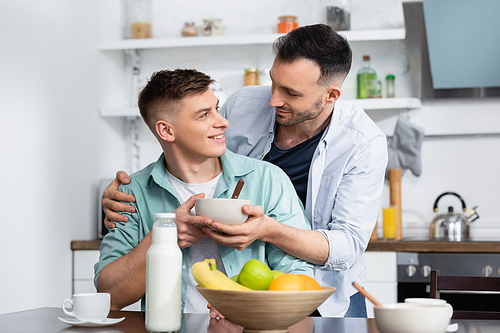 homosexual man holding bowl near husband and fruits on table