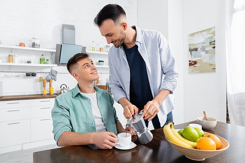 happy homosexual man pouring coffee near husband in kitchen