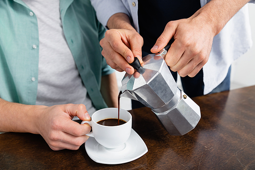cropped view of homosexual man pouring coffee in cup near husband