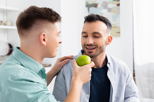 happy homosexual man feeding husband with green apple