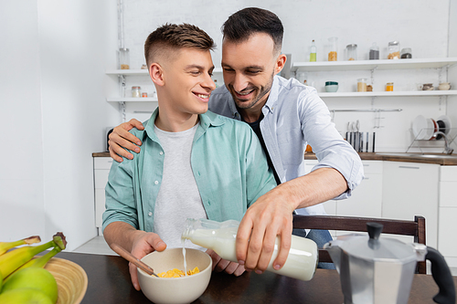 happy homosexual man pouring milk in bowl with corn flakes