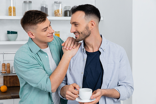 happy man holding saucer with cup of coffee and looking at husband
