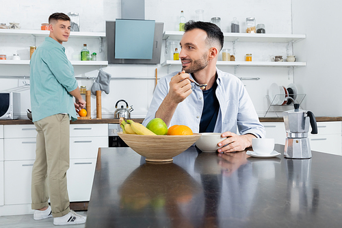 happy homosexual man eating corn flakes near husband on blurred background