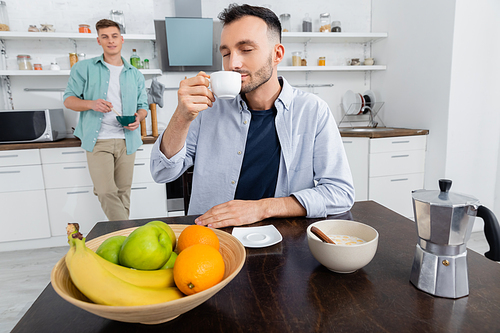 homosexual man drinking coffee near husband on blurred background
