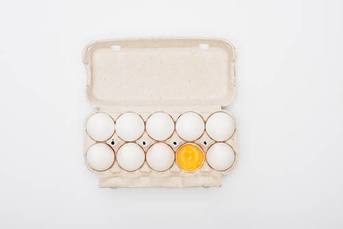 top view of fresh chicken eggs and yolk in cardboard box isolated on white