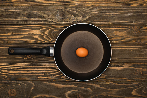 top view of raw chicken egg in frying pan on wooden surface