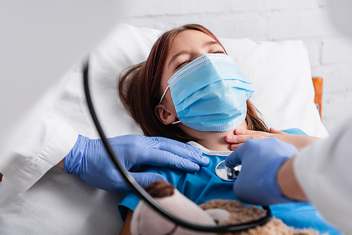 doctor examining girl, lying in medical mask with closed eyes, with stethoscope, blurred foreground