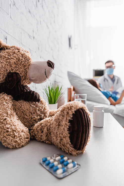 selective focus of teddy bear and pills near doctor and patient on blurred background