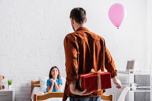 back view of man holding festive balloon and gift box near happy daughter on blurred background