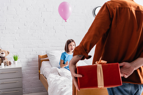 amazed child holding festive balloon near dad with gift box on blurred foreground
