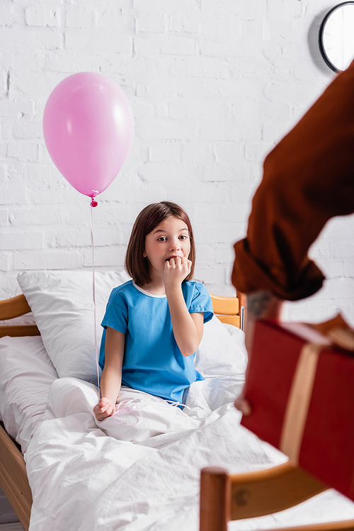 astonished girl holding festive balloon near father with gift box on blurred foreground