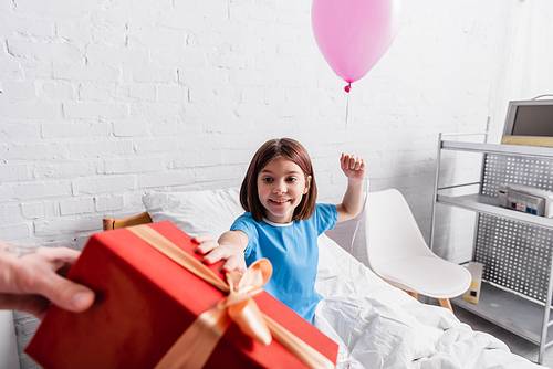 cheerful girl holding festive balloon near father with gift box on blurred foreground