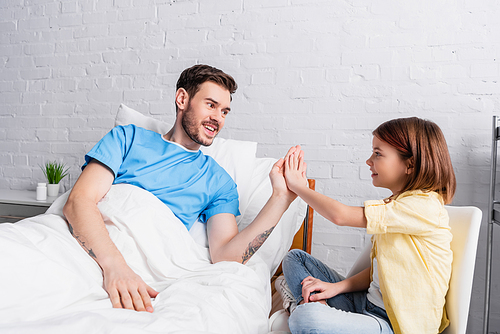 cheerful man giving high five to happy daughter in hospital