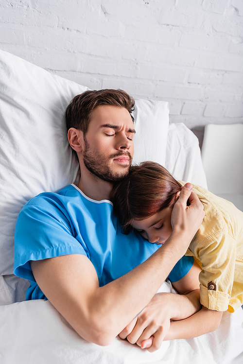 sick man embracing daughter while lying in hospital bed with closed eyes