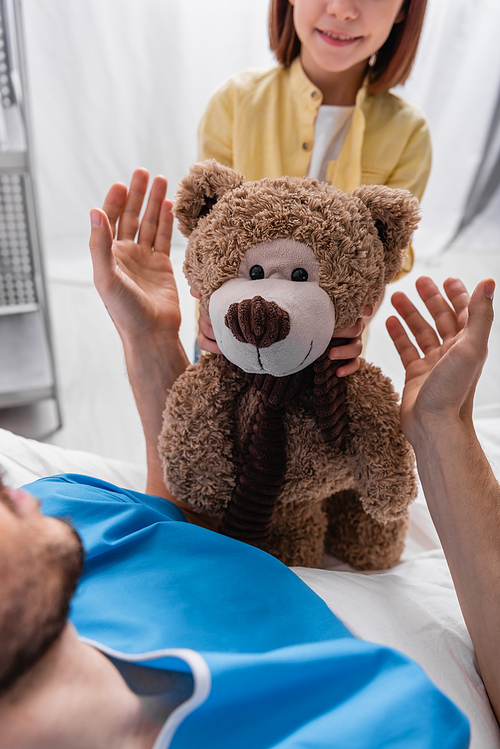 cropped view of child giving teddy bear to father lying in hospital