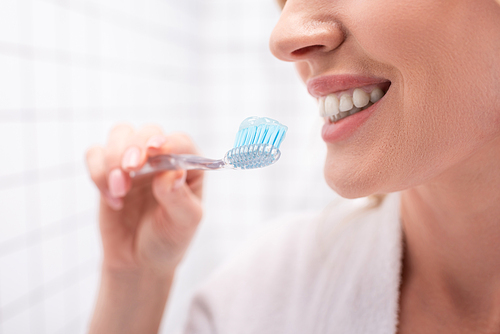 partial view of cheerful woman smiling while holding toothbrush with toothpaste