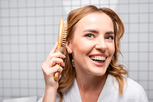 happy woman smiling and brushing hair in bathroom