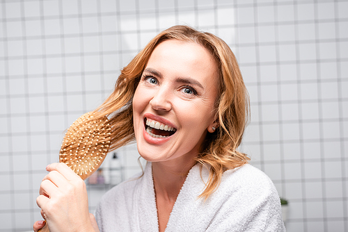 joyful woman smiling and brushing hair in bathroom