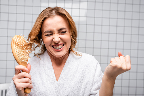 amazed woman in white bathrobe brushing hair in bathroom