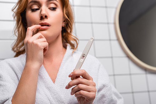 worried woman in bathrobe looking at pregnancy test in bathroom